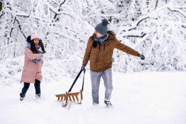 Sıcak giysiler atar kartopu kocası ve o onun elinde kızakları ile güzel bir hamile kadında ondan kaçar. Eğlenceli kış parkta.