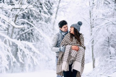 Genç adam şefkatle sıcak battaniye arka plan üzerinde kar yağışı ile kaplı güzel hamile karısını sarılmak. Aile sevgi ve bakım kavramı.