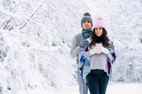 美丽的孕妇与她的丈夫穿着灰色针织毛衣 围巾和牛仔裤 拿着粉红色的茶杯与热茶和走在雪冬公园的背景 — 图库照片
