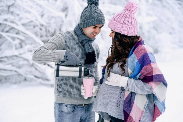 美丽的孕妇和她的丈夫走在雪公园 一个男人给他可爱的妻子倒温热的茶 — 图库照片