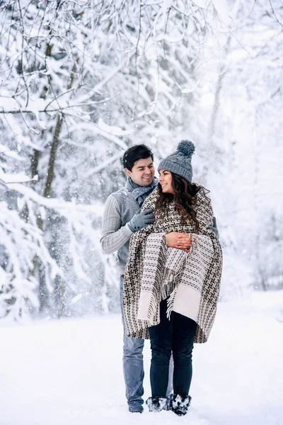 年轻人温柔地拥抱着他美丽怀孕的妻子 妻子被温暖的毯子覆盖着 背景是雪 家庭的爱和关怀概念 — 图库照片