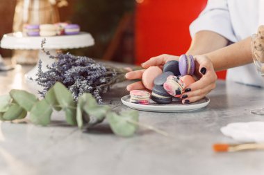 Baker'ın eller renkli macarons mermer bir tablo üzerinde beyaz bir tabak içine dökün.