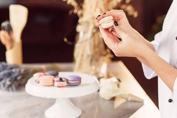 The confectioner joins the parts of the macarons with each other using a cream. Close up baker hands making macarons.