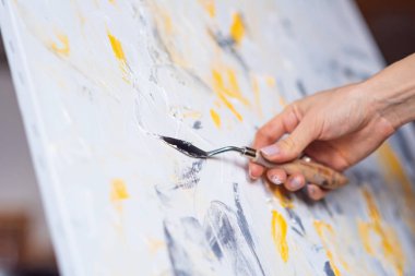 Sanatçının el Mastik ve sarı boya slaytlar beyaz tuval üzerine kapatın.