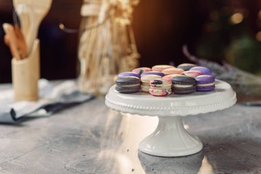 Arka planda bir peçete ve mutfak aksesuarları ile mermer bir tablo üzerinde beyaz bir tepsi üzerinde renkli macarons.