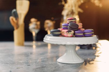 Arka planda bir peçete ve mutfak aksesuarları ile mermer bir tablo üzerinde beyaz bir tepsi üzerinde renkli macarons.