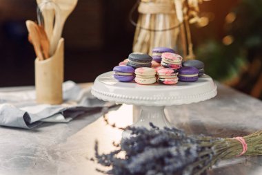 Bir peçete, lavanta ve mutfak aksesuarları ile mermer bir tabloda beyaz bir tepsi üzerinde renkli macarons.