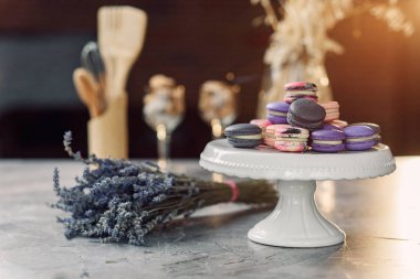 Bir peçete, lavanta ve mutfak aksesuarları ile mermer bir tabloda beyaz bir tepsi üzerinde renkli macarons.