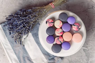 Bir peçete ve lavanta ile mermer tabloda üstten görünüm renkli macarons ile beyaz plaka. Lezzetli tatlı.