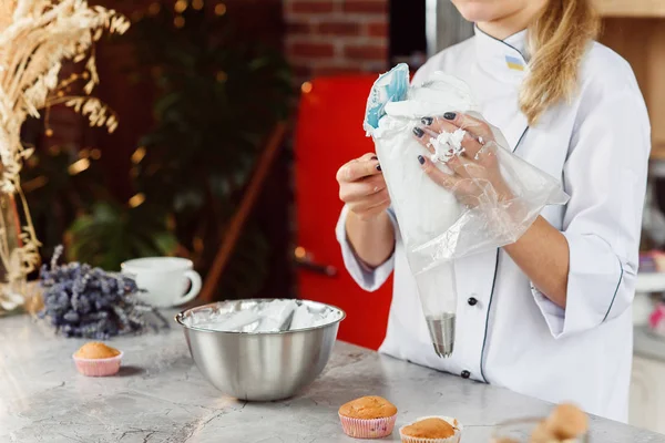 The female confectioner fills the confectionery bag with a freshly prepared cream.