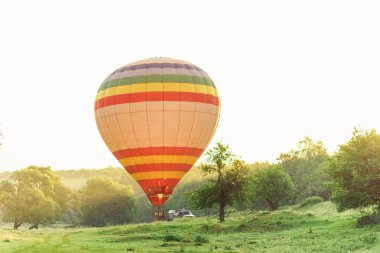 Seyahat ve spor. Yukarıda gökyüzü vadide güneş doğarken uçan çok renkli çizgili sıcak hava balonu.