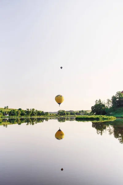 Travel and sport. Two multi colored hot air balloons flying above lake in sky at sunrise.