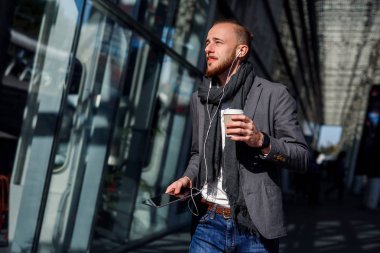 İş merkezine yakın bir çalışma öğle yemeği molası sırasında yürüyüş tablet bilgisayar istimal headphones ile beyaz iş adamı. Genç adam müzik veya sesli kitap dinler, mali çizelgeleri, kahve içme denetler.