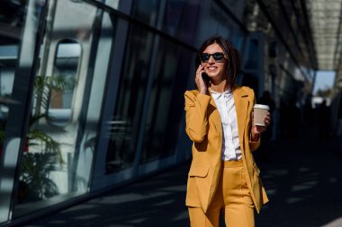 Gülümseyen iş kadını kenti, iş merkezine yakın yürüyüş sarı elbiseli smartphone iletişim kurar ve kahve içiyor. İş kavramı, iletişim, bankacı, Yöneticisi ve ofis işçi.