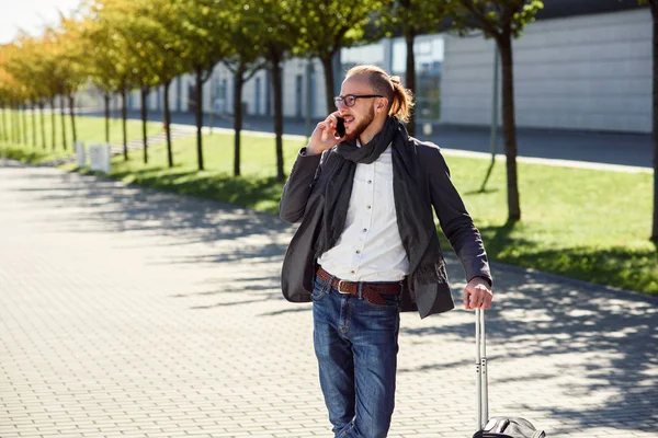 Başarılı bir iş adamı rahat kıyafetli bir bavul, Havaalanı ve akıllı telefon üzerinde görüşmeler için acele çeker. İş gezisine giden genç beyaz adam.