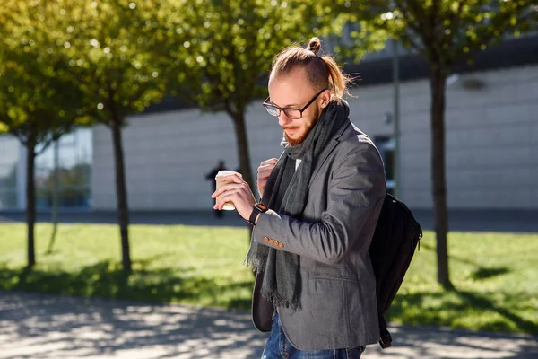 Genç başarılı iş adamı eşarp yürüyüşler ve iş merkezine yakın gri bir ceket kahve içiyor ve nöbetlere arıyorum. İş, bankacı, Yöneticisi kavramı.