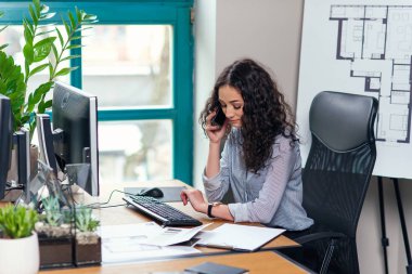 Genç kadın iç tasarımcı akıllı telefonda konuşan ve izlemek için iş günü içinde modern ofis.