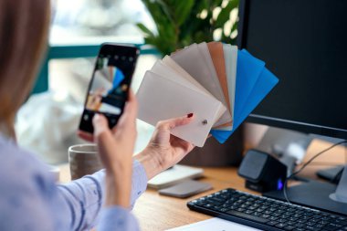 Kadın tasarımcı renk örnekleri ile çalışma ofisinde. İşyerinde kadın bir fotoğraf renk paletinin Smartphone'da yapar..