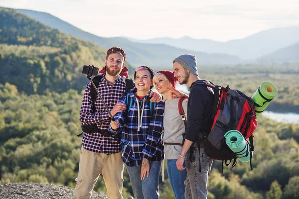 Grupo de jóvenes sonrientes viajando juntos en las montañas. Felices viajeros hipster con mochilas haciendo selfie. Concepto de viaje, turismo y amistad . — Foto de Stock