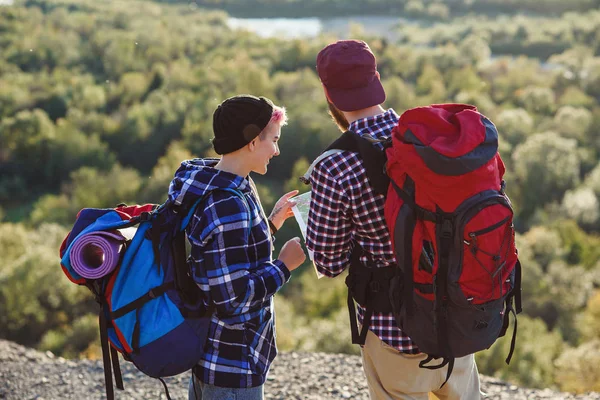 Jong koppel samen reizen in bergen. Gelukkig hipster man en zijn vriendin met rugzakken planning van de route door papieren kaart te bekijken. Reizen, toerisme en vriendschap concept. — Stockfoto