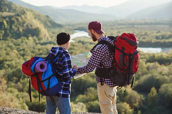 Pareja joven viajando juntos en las montañas. Feliz hombre hipster y su novia con mochilas planeando ruta mirando el mapa de papel. Concepto de viaje, turismo y amistad . — Foto de Stock