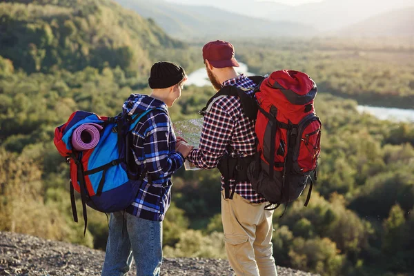 Young couple traveling together in mountains. Happy hipster man and his girlfriend with backpacks planning route by looking at paper map. Traveling, tourism and friendship concept.