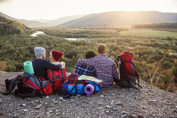 Grupo de jóvenes amigos que viajan juntos en las montañas. Felices viajeros hipster con mochilas sentadas en la cima de la montaña al atardecer. Concepto de viaje, turismo y amistad . — Foto de Stock