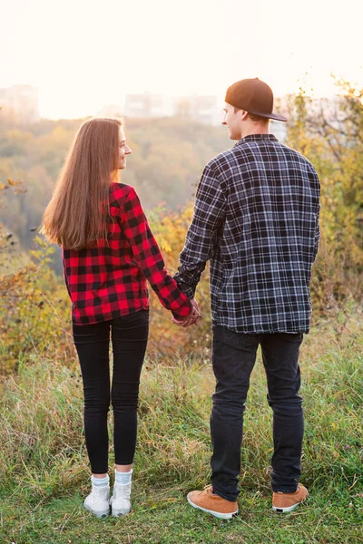 Cerca de un joven y su novia en ropa casual sostiene las manos el uno al otro. Pareja feliz con guitarra descansando en el picnic en el parque . — Foto de Stock