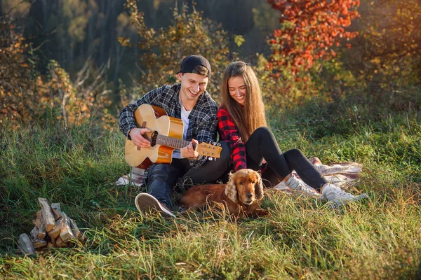 Felice bella coppia in abiti casual con chitarra e il loro cane avendo riposo sul pic-nic nel parco . — Foto Stock