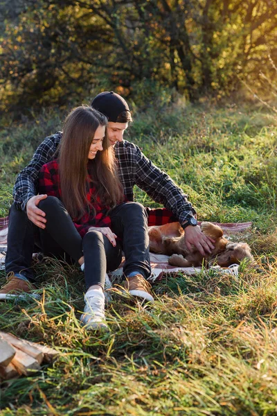 Felice coppia caucasica con chitarra a riposo su picnic nel parco primaverile. Giovane uomo e la sua ragazza giocare con il loro cane divertente . — Foto Stock