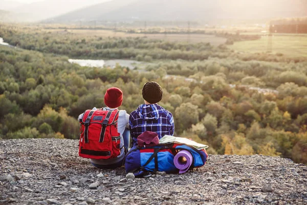 Dos amigos viajando juntos en las montañas. Viajeros femeninos hipster felices con mochilas y un mapa sentado en la cima de la montaña al atardecer. Concepto de viaje, turismo y amistad . — Foto de Stock