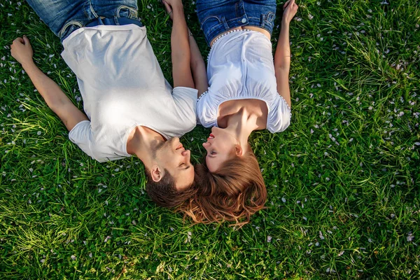 Pareja romántica de jóvenes tendidos en el césped en el parque. Se ponen uno sobre los hombros del otro y se agarran de las manos. Parecen felices. Vista desde arriba . — Foto de Stock