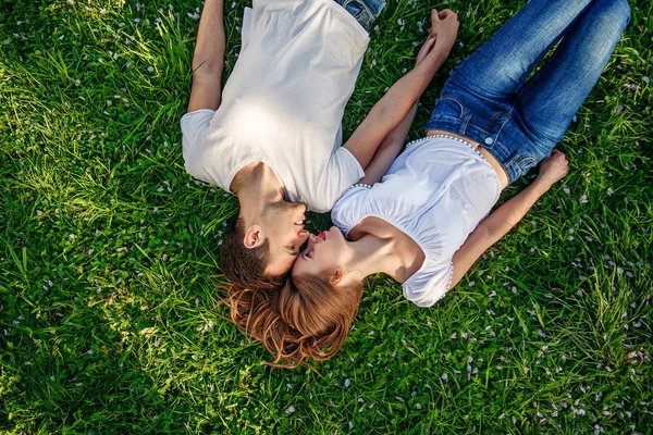 Pareja romántica de jóvenes tendidos en el césped en el parque. Se ponen uno sobre los hombros del otro y se agarran de las manos. Parecen felices. Vista desde arriba . —  Fotos de Stock