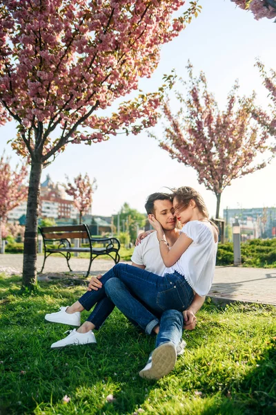 Abbracci di coppia vicino ad alberi di sakura in giardino fiorente. La coppia innamorata passa il tempo in giardino di primavera, fiori su sfondo, vicino. Passione e amore concetto . — Foto Stock