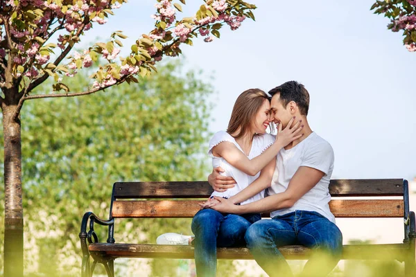 Abbracci di coppia vicino ad alberi di sakura in giardino fiorente. La coppia innamorata passa il tempo in giardino di primavera, fiori su sfondo, vicino. Passione e amore concetto . — Foto Stock