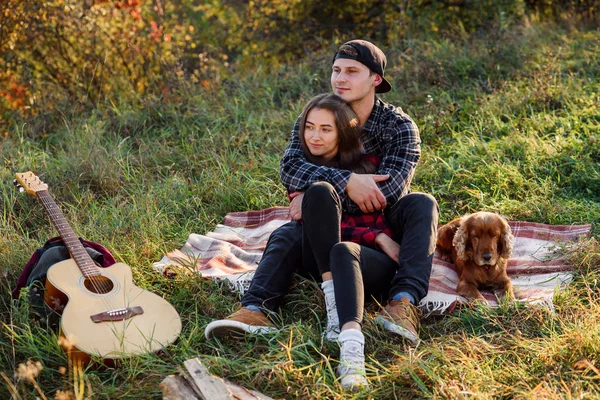 Felice coppia caucasica con il cane seduto sul prato nel parco primaverile. Giovane uomo e la sua ragazza godendo della natura . — Foto Stock