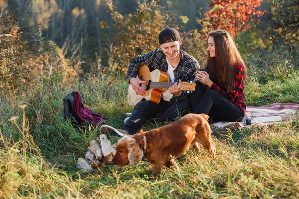 Ung man som spelar på gitarren för hans vackra flickvän. Lyckliga par med gitarr som vilar på picknick i vår park. — Stockfoto