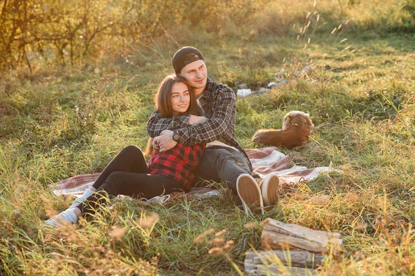 Giovane uomo abbraccia teneramente la sua bella ragazza. Giovane coppia si siede sul plaid a prato verde al tramonto . — Foto Stock