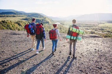 Üzerinden dört hipster arkasında el ele tutuşarak ve ileri Dağı'na günbatımı arka planda çalışan seyahat sırt çantası ile görüntüle.