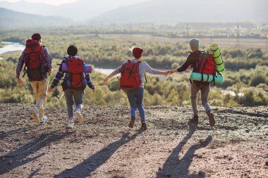 Üzerinden dört hipster arkasında el ele tutuşarak ve ileri Dağı'na günbatımı arka planda çalışan seyahat sırt çantası ile görüntüle.