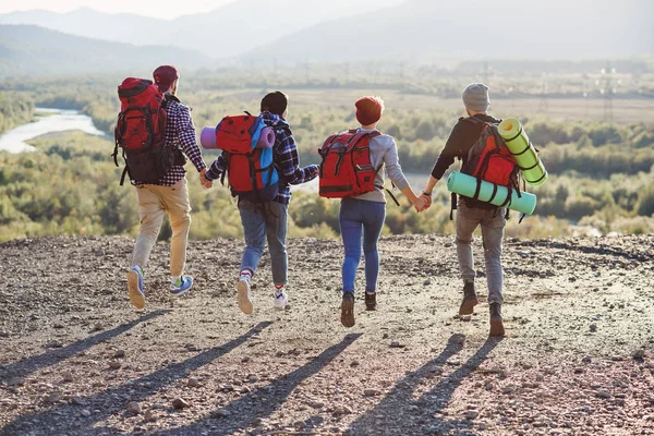 Üzerinden dört hipster arkasında el ele tutuşarak ve ileri Dağı'na günbatımı arka planda çalışan seyahat sırt çantası ile görüntüle.