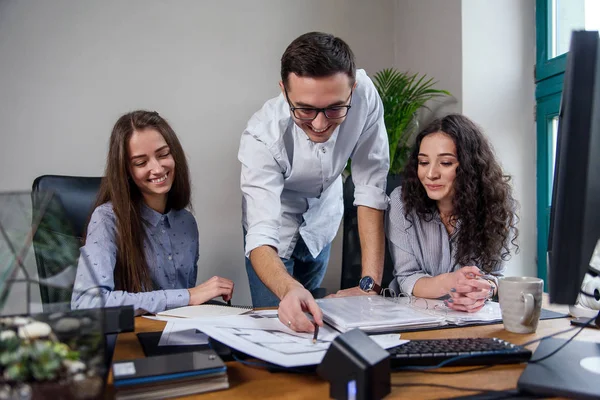 Guapo gerente de la firma en gafas explica las tareas de trabajo para sus empleados. Gente creativa o concepto de negocio publicitario. Trabajo en equipo. Jóvenes hermosas personas que trabajan juntos en la oficina . — Foto de Stock