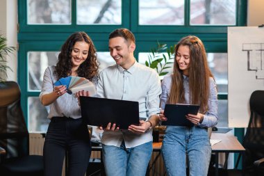 Genç Beyaz Mimarlar veya arka plan üzerinde büyük pencere ile şık modern ofis içinde belgili tanımlık laptop üzerinde yeni projesi için renk paletini kullanarak tasarımcılar.