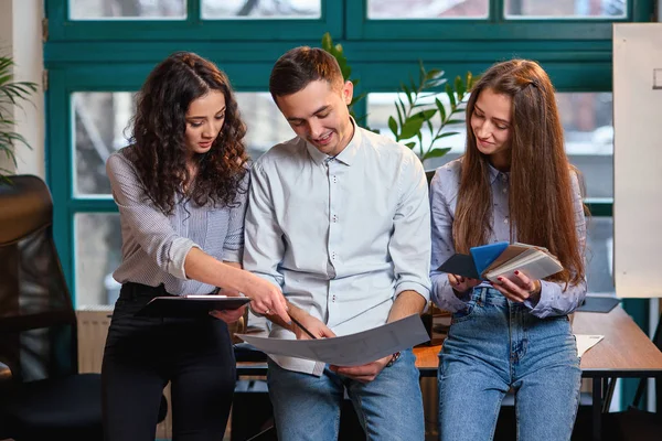 Equipo exitoso de jóvenes ingenieros caucásicos de pie cerca de una mesa de madera y hablando de un nuevo proyecto. Concepto empresarial . — Foto de Stock