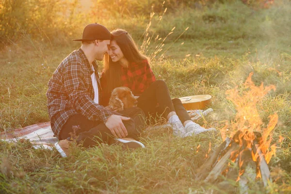 Feliz casal caucasiano em roupas casuais com seu cão engraçado sentado no gramado no parque da primavera. Jovem menina bonita e seu namorado bonito se apoiaram uns contra os outros na natureza . — Fotografia de Stock