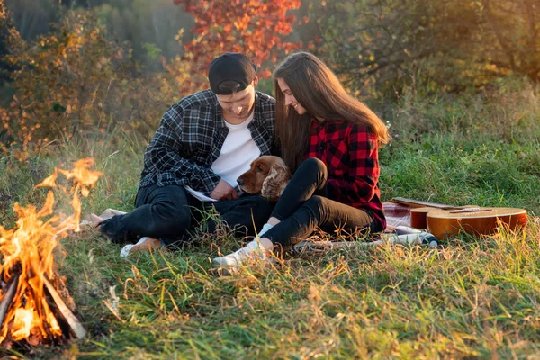 Felice coppia caucasica con il cane seduto sul prato nel parco primaverile. Giovane uomo e la sua ragazza godendo della natura . — Foto Stock