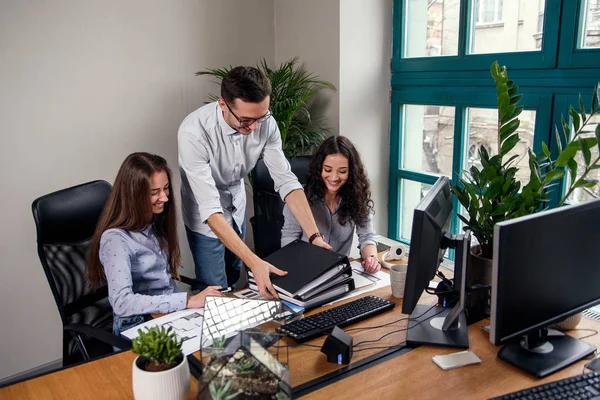 Dos mujeres hermosas que trabajan en el proyecto de arquitecto en la oficina moderna, mientras que el hombre con camisa elegante traer carpetas de documentos . — Foto de Stock