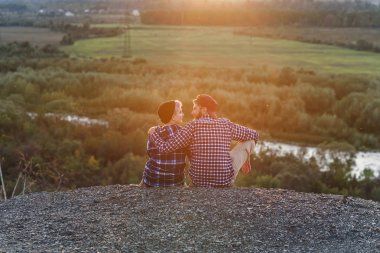 Dağın tepesinde oturan ve gün batımında birbirlerine bakan genç çift... Romantik günbatımında nazik bir çift.
