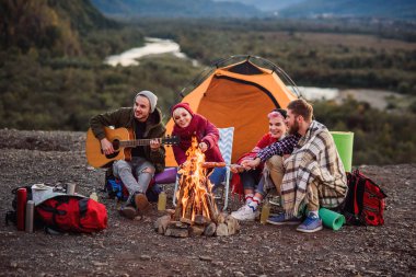 Mutlu arkadaşlar dağlarda piknik yapıyor, sohbet ediyorlar, enerji içecekleri içiyorlar, gitar çalıyorlar ve kamp ateşinde sosis pişiriliyorlar. Mutluluk kavramı, gençlik ve yaşam keyfi.
