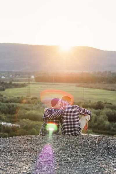 Egy fiatal pár szerelmes ül egymás ellen a tetején a hegy naplementekor. Gyengéd pár romantikus naplemente háttérben. — Stock Fotó